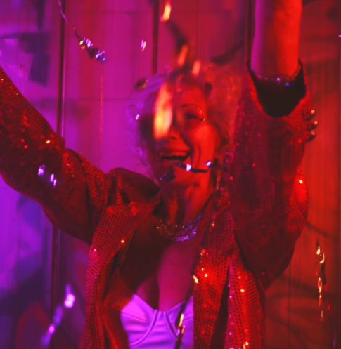 Kvinna i festkläder dansar under konfetti i färgglatt ljus