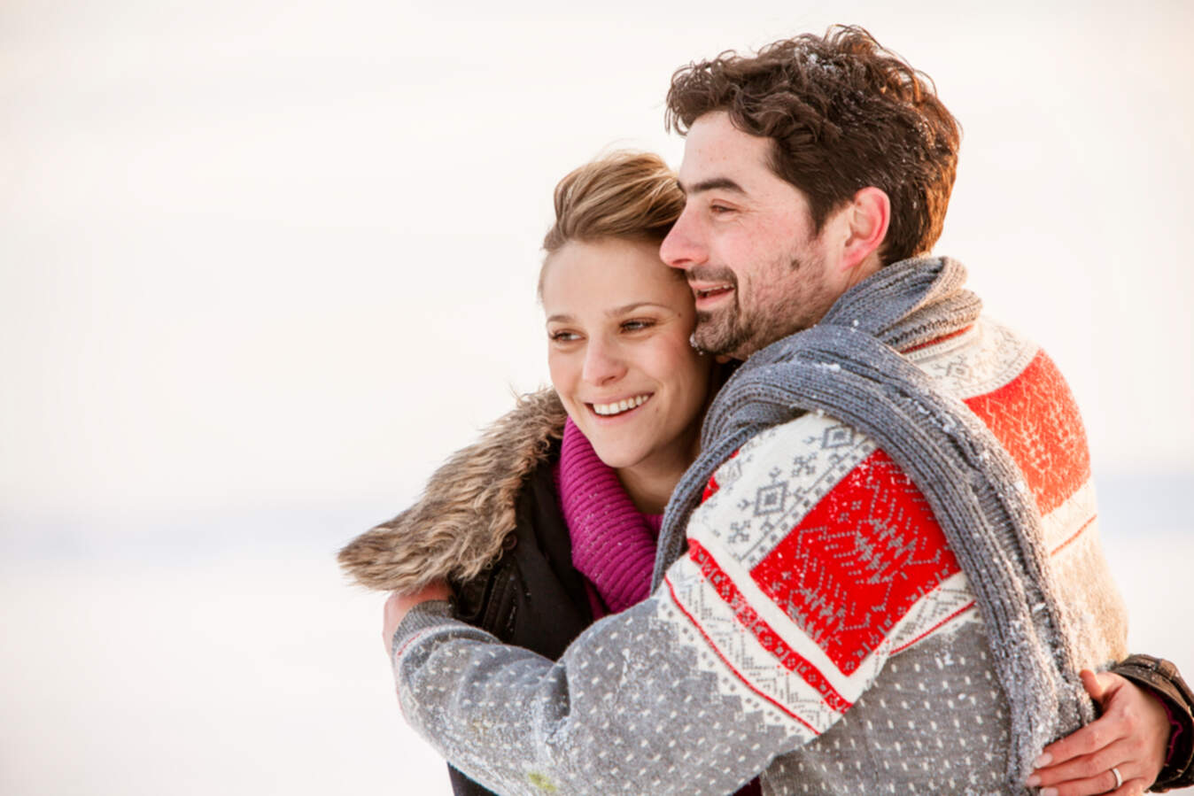 Ungt par som kramas utomhus i vintermiljö, klädda i varma vinterkläder