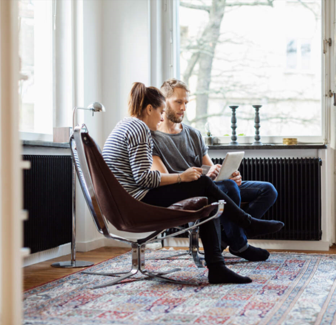 Personer samarbetar vid en bärbar dator i ett modernt vardagsrum med stora fönster och dekorativ matta