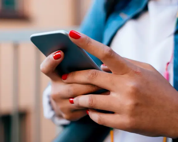 Person använder en smartphone med rött nagellack på naglarna, fokus på händerna