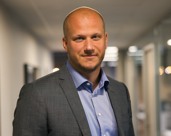 Man i kostym i kontorsmiljö, kortklippt och leende, med suddig bakgrund