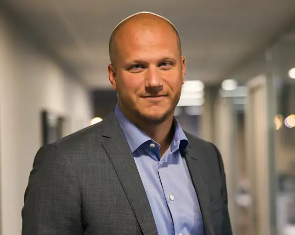 Man i kostym i kontorsmiljö, kortklippt och leende, med suddig bakgrund