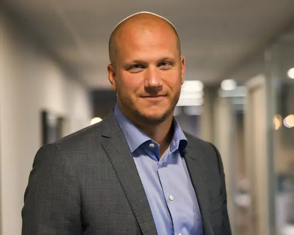 Man i kostym i kontorsmiljö, kortklippt och leende, med suddig bakgrund