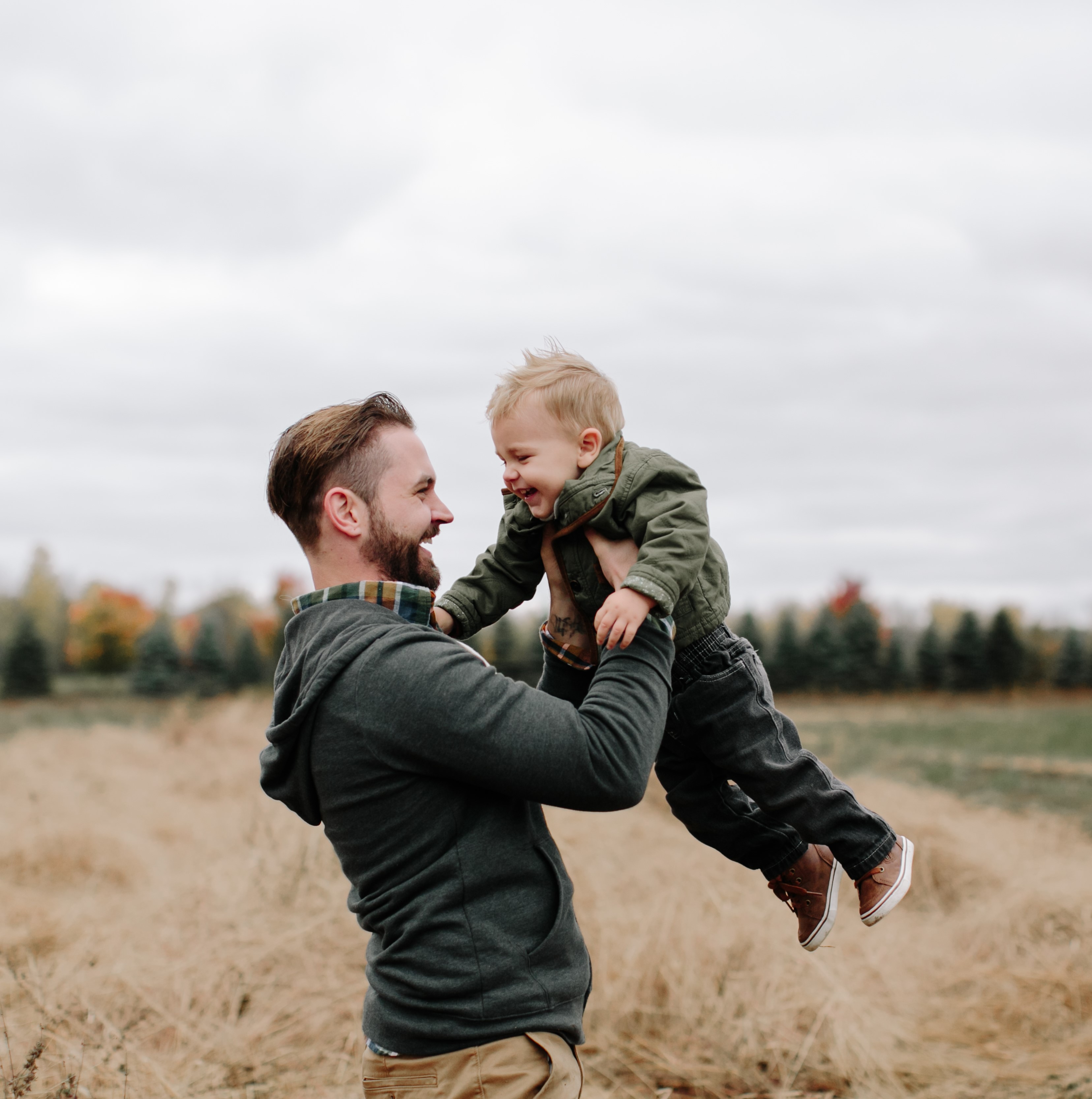 Man lyfter upp ett leende barn i en höstlig utomhusmiljö med träd i bakgrunden