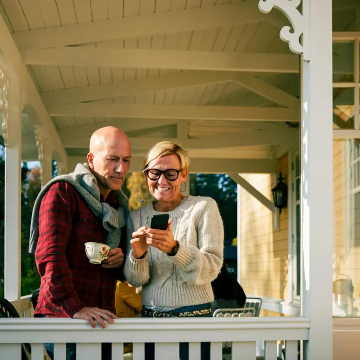 Par på veranda som tittar på en mobiltelefon, njuter av soligt väder