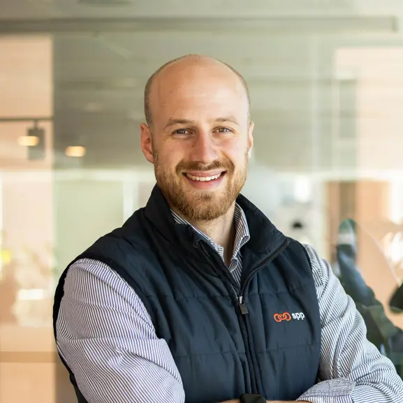 Man i kontorsmiljö med svart väst och randig skjorta, ler mot kameran