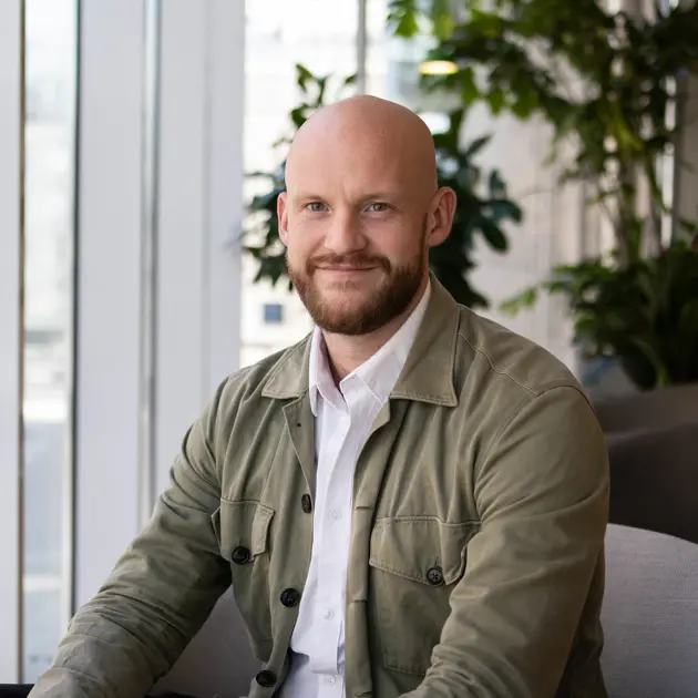 Man i grön jacka och vit skjorta sitter i en modern kontorsmiljö med gröna växter i bakgrunden