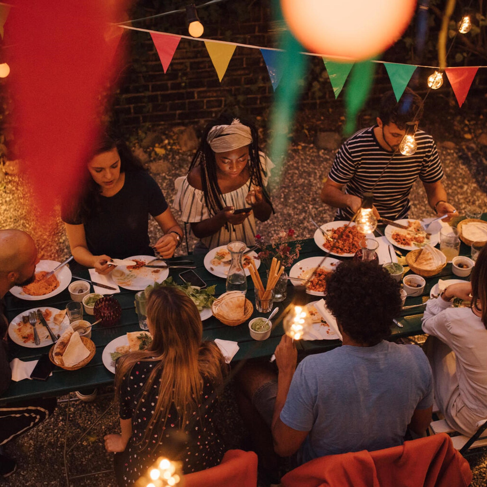 Grupp människor som delar en måltid utomhus under festliga ljusslingor och färgglada vimplar