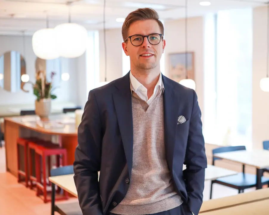 Man i kostym och glasögon i modernt kontorsmiljö med bord och stolar i bakgrunden