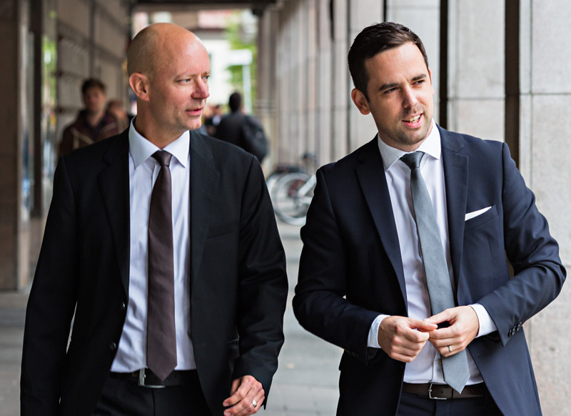 Två affärsmän i kostym går och samtalar utomhus i en stadsmiljö i dagsljus