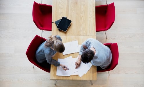 Två personer diskuterar över ett bord med dokument och surfplatta i en kontorsmiljö
