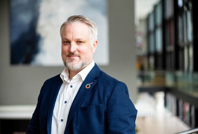 Man i blå kavaj står inomhus med suddig bakgrund