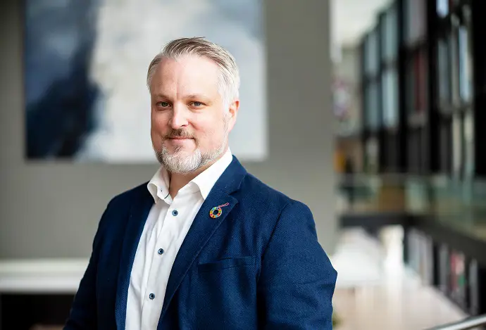 Man i blå kavaj står inomhus med suddig bakgrund