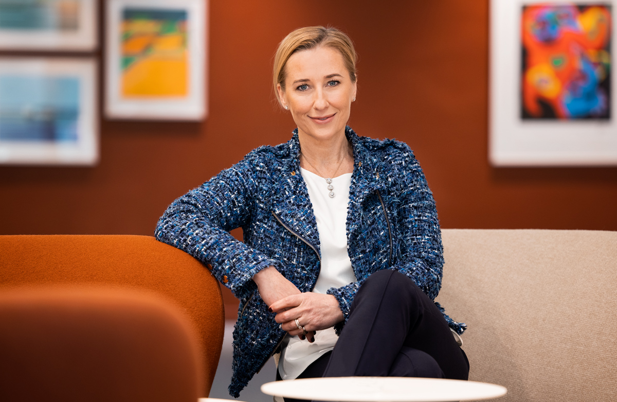 Kvinna i blå jacka sitter i ett modernt konstgalleri med färgglada tavlor i bakgrunden