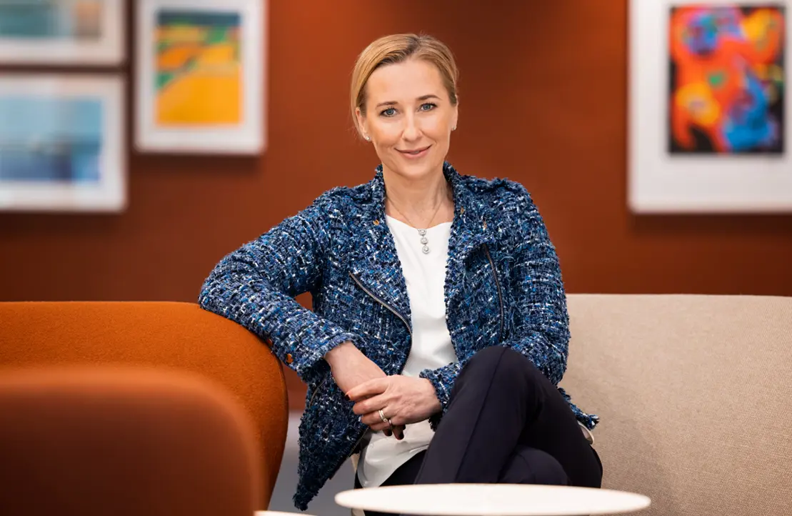 Kvinna i blå jacka sitter i ett modernt konstgalleri med färgglada tavlor i bakgrunden