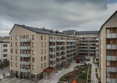 Moderna lägenhetsbyggnader i ett bostadsområde med innergård och lekplats under molnig himmel