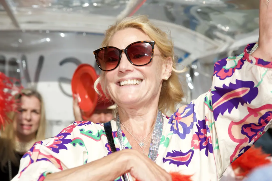 Kvinna i solglasögon och blommig blus ler glatt under en utomhusevenemang