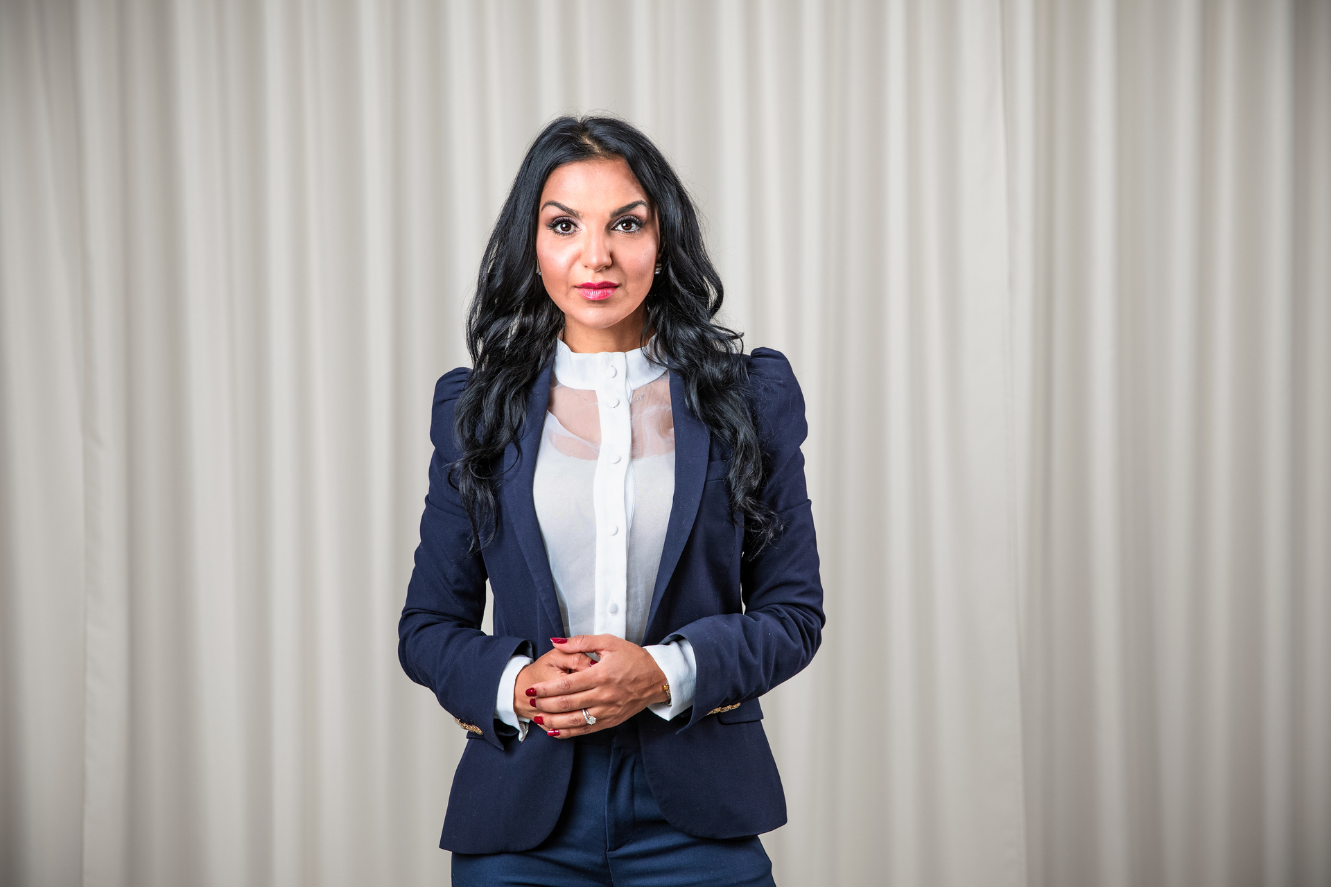 Kvinna i blå kostym framför ljusa gardiner