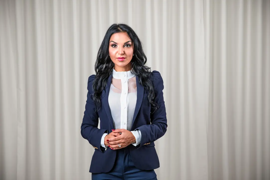 Kvinna i blå kostym framför ljusa gardiner