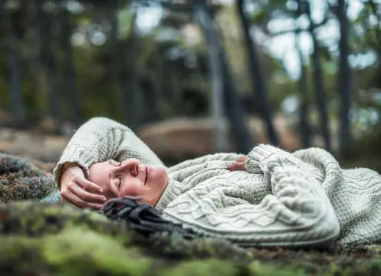 Man i tjockstickad tröja ligger avslappnad på mossa i skogen