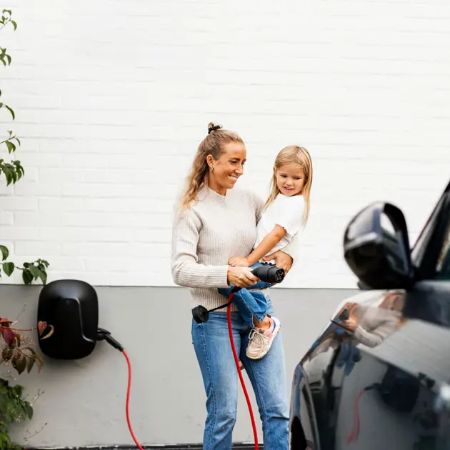 Kvinna med barn laddar elbil utomhus mot vit tegelvägg