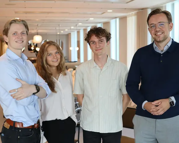 Fyra leende personer stående i ett modernt kontor, alla i avslappnad klädsel