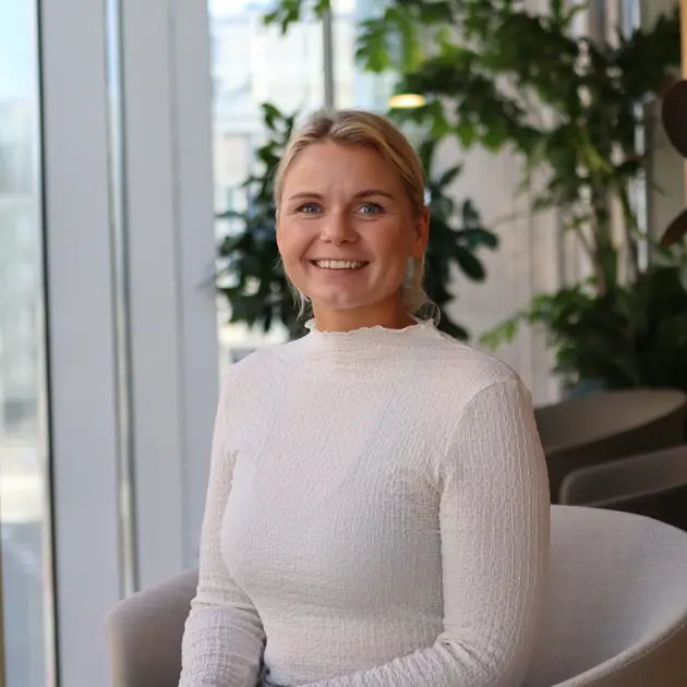 Kvinna i vit tröja sitter i en modern kontorsmiljö med gröna växter i bakgrunden