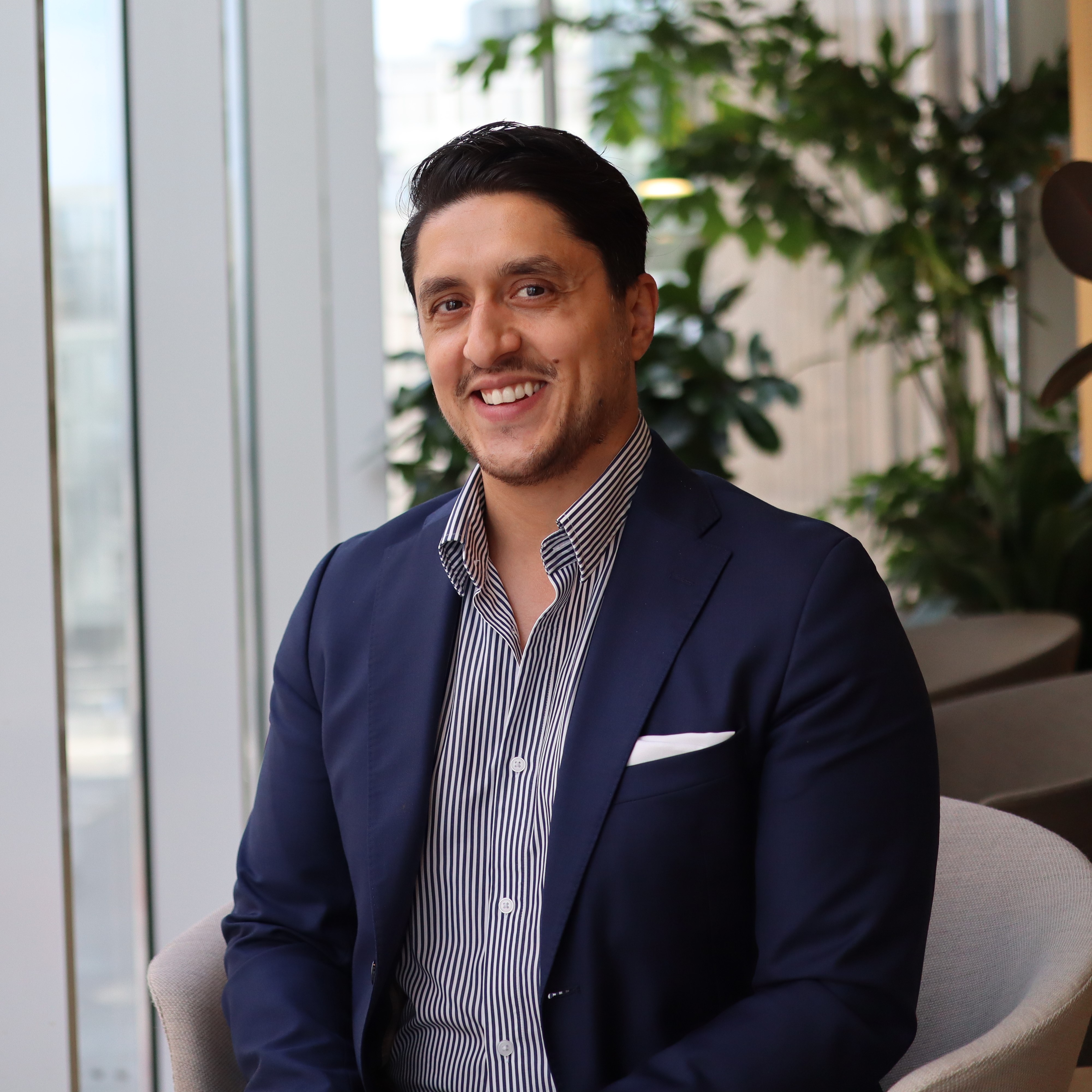 Man i blå kostym sitter i modernt kontor med grönska i bakgrunden