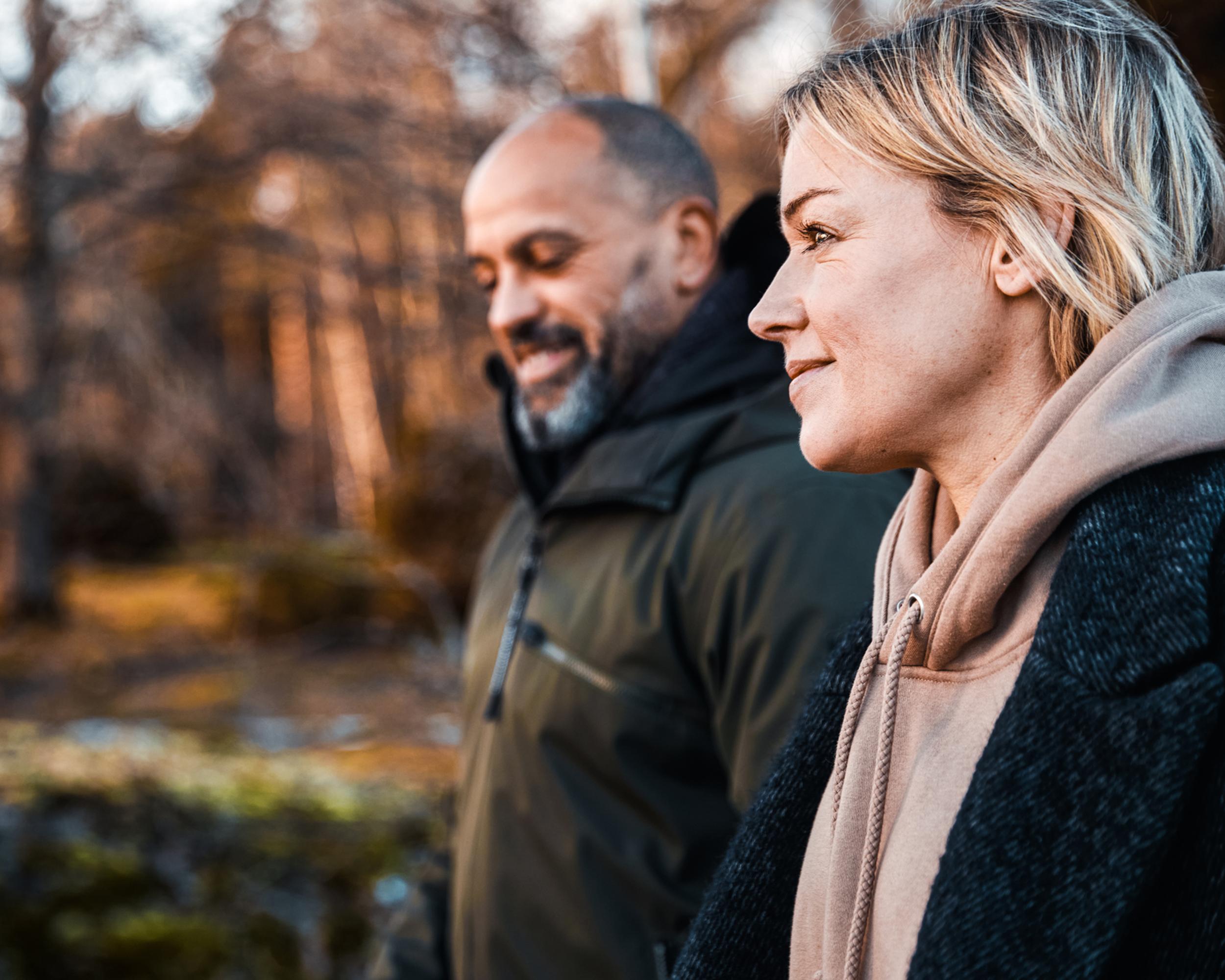 Två personer som promenerar i skogen under hösten, iklädda varma kläder