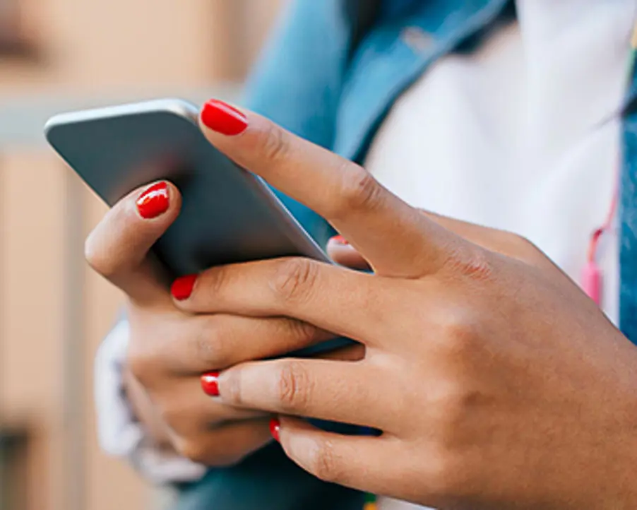 Person använder mobiltelefon med rödmålade naglar, klädd i blå jacka och vit skjorta, fokus på händer och teknologi