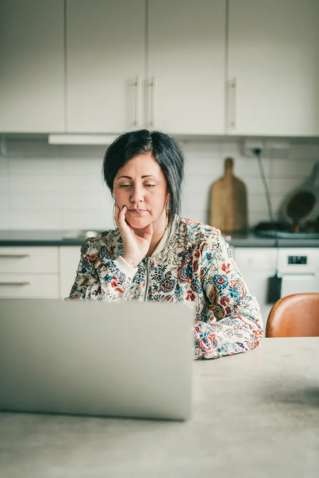 Kvinna i färgglad tröja arbetar fokuserat vid datorn i modernt kök