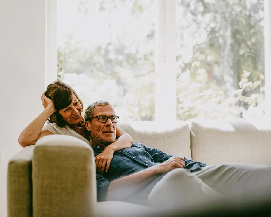 Äldre par kramas på en soffa i ett ljust vardagsrum