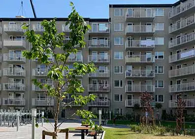 Modernt flerfamiljshus med balkonger och grön gård i förgrunden, ljus dag