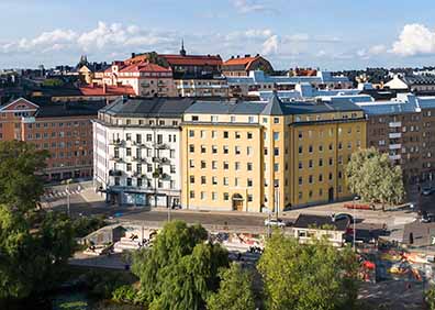 Vy över stadsgata med färgglada byggnader i centrala Stockholm, omgivna av grönska och blå himmel