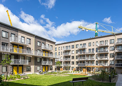 Modern bostadsområde med lägenhetsbyggnader och gröna innergårdar under blå himmel, byggkranar i bakgrunden