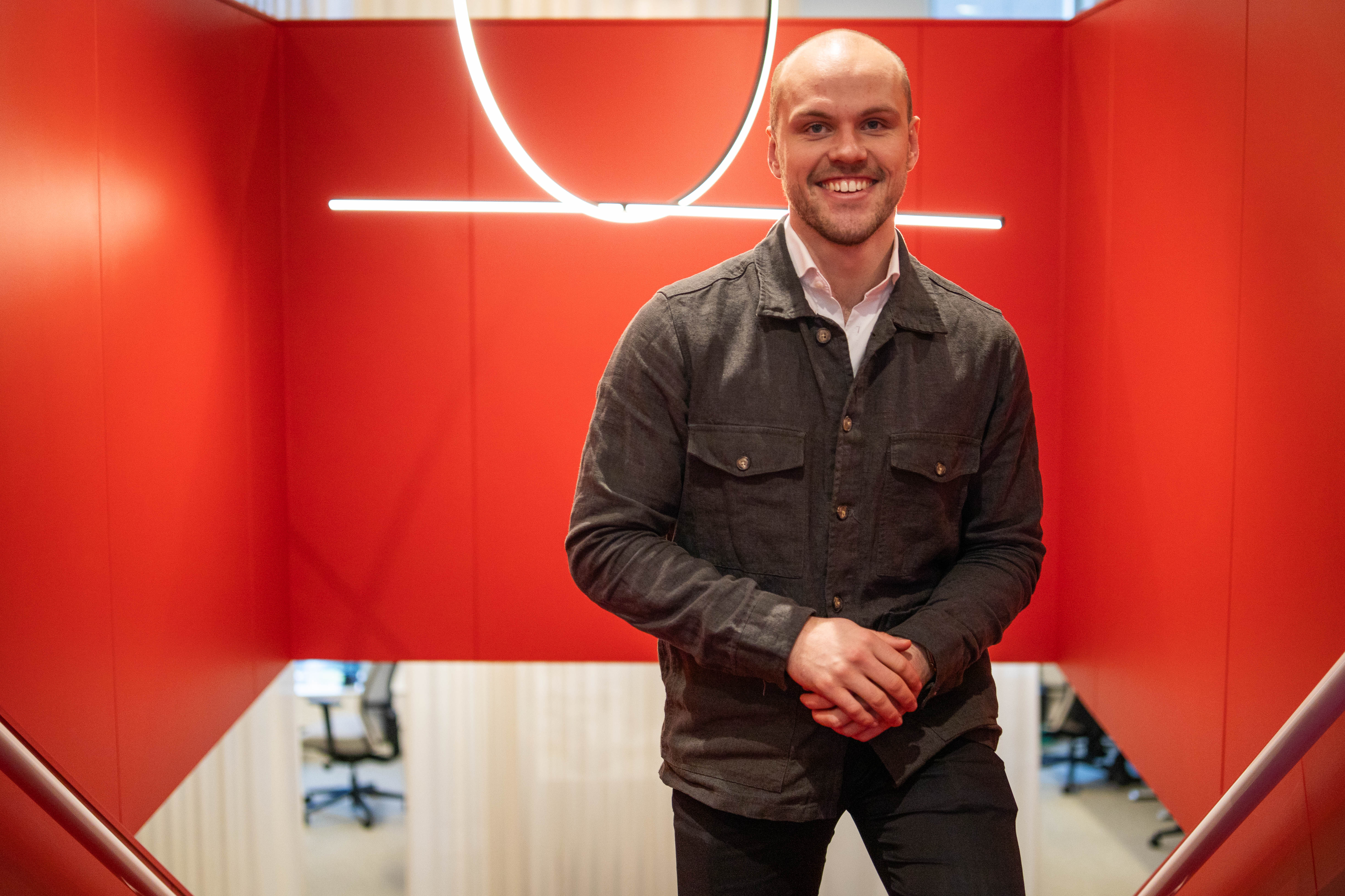 Man i casual kavaj står i en röd inomhusmiljö. Ljuskrona i bakgrunden