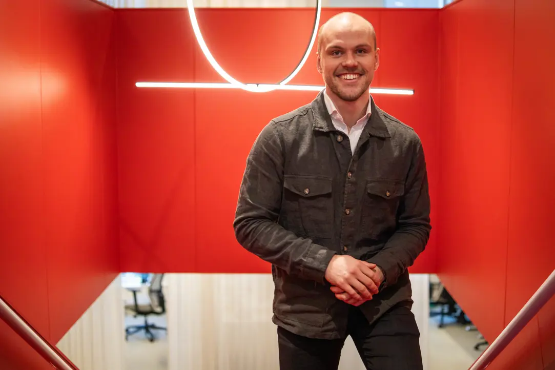 Man i casual kavaj står i en röd inomhusmiljö. Ljuskrona i bakgrunden