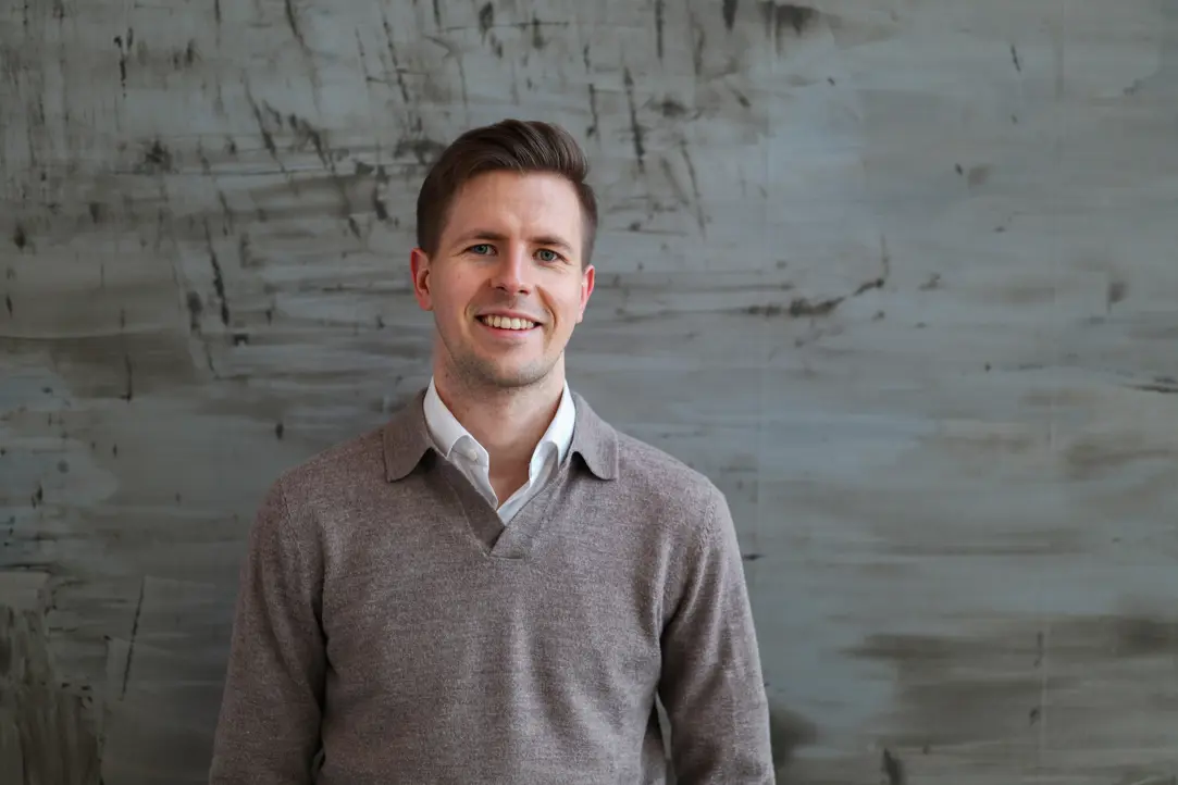 Man i grå tröja ler framför en grå vägg